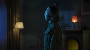 Daire yaratıcı konseptinde korku filmi sahnesi. Beyaz hokey maskeli adam karanlık oturma odasında yürüyor, etrafa bakıyor, kızı arıyor, elinde bıçak ile poz veriyor. HDR BT2020 HLG Malzemesi