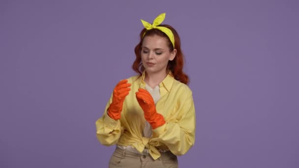 クリーニングとハウスキーピングのクリエイティブコンセプト カジュアルな服とゴム手袋の女性は 交差した手でポーズ 笑顔の表情 カメラを見ています 紫色の背景に隔離される — ストック動画