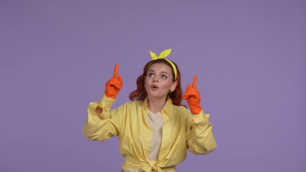 クリーニングとハウスキーピングのクリエイティブコンセプト カジュアルな服とゴム製の手袋の女性は 上部に手をつないで指を指差し カメラに微笑みました 紫色の背景に隔離される — ストック動画