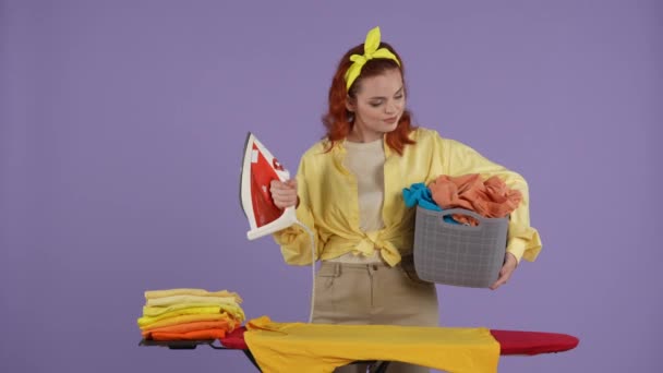 清洁和家政创意的概念 穿着休闲装的女人手里拿着铁和装满衣服的篮子 站在熨烫板旁边 满脸笑容 被紫色背景隔离 — 图库视频影像