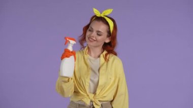Temizlik ve temizlik yaratıcı konsepti. Günlük kıyafetler giymiş, lastik eldivenli, elinde temizleyici sprey, elinde bez parçasıyla gülümseyen bir kadın resmi. Mor arkaplanda izole.