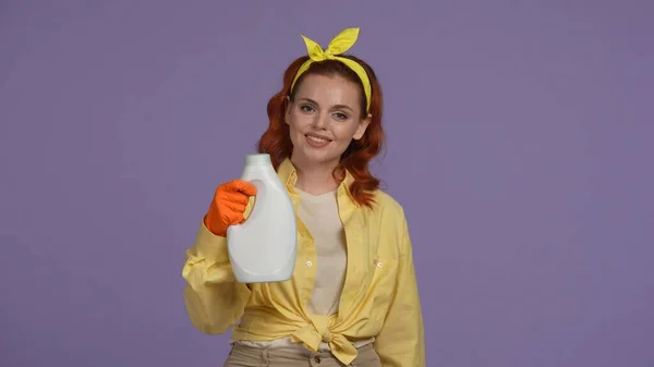 毎日の清掃とハウスキーピングのコンセプト カジュアルな服とゴム手袋の女性は 生地軟化剤のボトルを保持し カメラを宣伝し 紫色の背景に隔離される — ストック写真