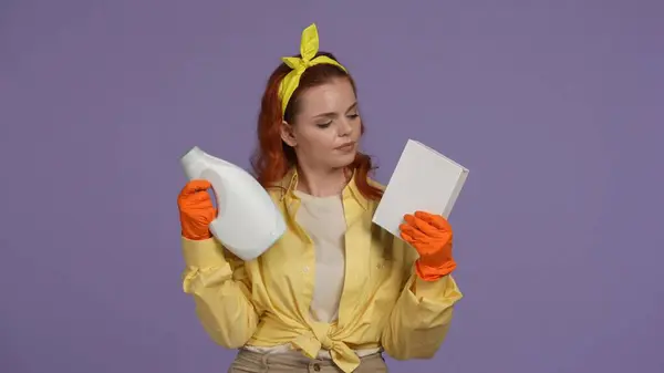 日常清洁和家务事的概念 穿着休闲装和橡胶手套的女人拿着一盒洗衣粉和瓶子 在它们之间做出选择 被紫色背景隔离 — 图库照片