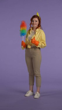 Her gün ev idaresi yaratıcı konsepti. Dikey fotoğraf. Günlük giysiler ve lastik eldivenler giymiş bir kadın piduster tutuyor, kameraya başparmaklarını gösteriyor, gülen yüz ifadesi var..