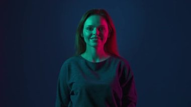 Stüdyoda, pembe ve yeşil neon ışıklı mavi arka planda genç kızıl saçlı bir kadının portresi. Baş parmak gösteren kadın