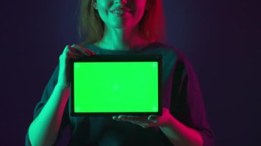 Pembe ve yeşil neon ışıklı bir stüdyoda bir kadının elinde yeşil ekranlı bir tablet.