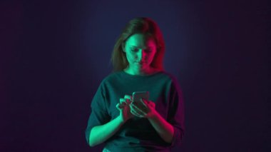 Genç kızıl saçlı bir kadın akıllı telefondan bir mesaj yazıyor, sosyal ağlar üzerinden yayınına bakıyor, iletişim kuruyor, iyi bir jest gösteriyor. Stüdyoda pembe ve yeşil neon ışıklarla aydınlatılmış bir kadın...