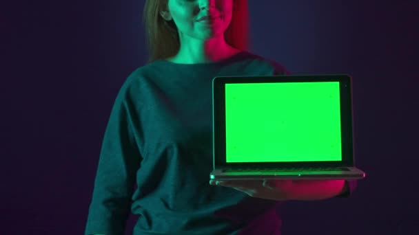 ピンクと緑のネオンライトのスタジオで女性の手の緑色のスクリーンとラップトップが閉じます 女性は緑色のラップトップのスクリーンで指を指差し 親指を示します — ストック動画