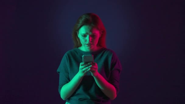一个兴奋的女人紧张而期待地看着智能手机屏幕 女人欢声笑语 做了一个胜利的手势 在工作室里拿着电话的蓝色女人 — 图库视频影像