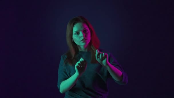 一个年轻的女人用手指和手在看不见的屏幕上打转 画室里一个女人的画像 蓝色背景 粉色和绿色霓虹灯 未来主义技术 — 图库视频影像