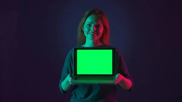 女性展示的笔记本电脑绿色屏幕关闭 一个女人的肖像 她的笔记本电脑在工作室里有一个绿色屏幕 蓝色背景上有粉色和绿色霓虹灯 广告领域 工作场所 — 图库照片