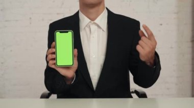 Yakın çekim, masada oturan tanınmayan bir gencin ayrıntılı videosu, elinde reklam alanı olan bir akıllı telefon, çalışma alanı modeli ve onay veren. İş ilanı, uygulama.