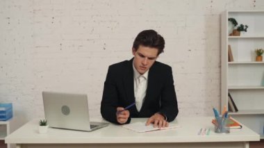 Ofisteki masada oturan genç bir adamın orta boy videosu. Bir şeyler yazıyor, üstünü çiziyor ve çarşafı yırtıyor, stresli, sinirli ve sinirli. İş, kariyer büyümesi, reklam.