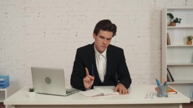 Ofisteki masada oturan genç bir adamın orta boy videosu. Bir fikir düşünüyor, bir şeyler yazıyor ve kameraya bakıyor, endişeli ve emin değil. İş, kariyer büyümesi, reklam.