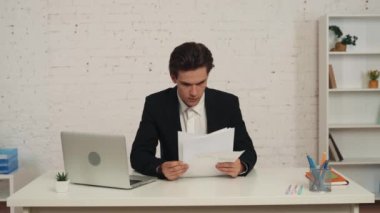 Ofiste oturan genç bir adamın masasındaki grafikleri ve çizelgeleri kontrol ederken çekilmiş orta boy videosu. Bir fikri var, kameraya bakıyor, mutlu ve kendinden emin. İş, kariyer büyümesi, reklam.