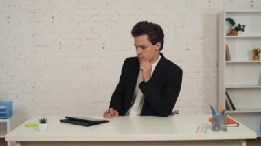 Ofisindeki masasında oturan genç bir adamın orta boy videosu. Tablette çalışıyor ve yön bulmak için stil ve kalem kullanıyor. Modern teknolojiler, fırsatlar, elektronik cihazlar, reklamlar.