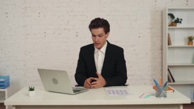 Ofiste dizüstü bilgisayarının önünde oturan genç bir adamın video görüntüsü. Konuşmaya başlıyor, biriyle konuşuyor, grafikler ve çizelgeler gösteriyor. İş, web kaynakları, uygulama.