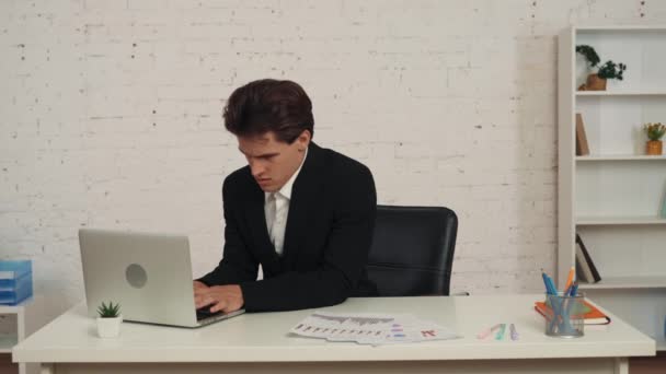 一个年轻人坐在桌边 在笔记本电脑上工作 然后伸展着身子 就好像他的背在漫长的一天之后受伤了一样 过度工作 健康问题 久坐不动的生活方式 — 图库视频影像