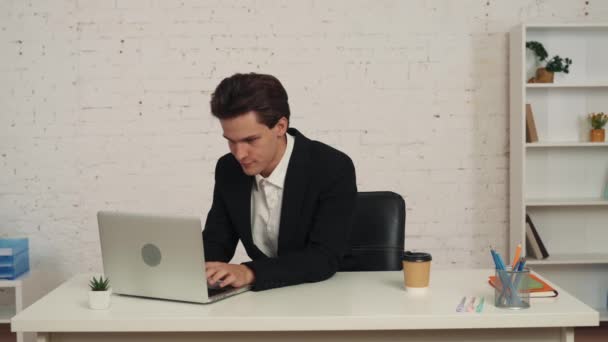 一个年轻人坐在办公室里的中等视频 他在笔记本电脑上工作 喝了一小口咖啡 做了个鬼脸 喘不过气来 好像饮料变质了似的 饮食服务 — 图库视频影像