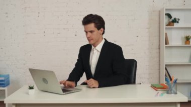 Bilgisayarının önünde oturmuş video aramasını bekleyen genç bir adamın orta boy videosu. Sonra konuşmaya başlıyor, biriyle konuşuyor, mutlu ve pozitif. İş, web kaynakları, uygulama.