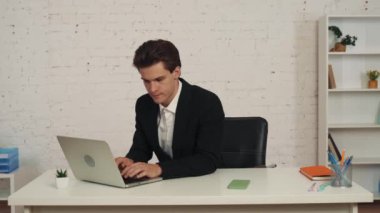 Ofiste dizüstü bilgisayarda çalışan genç bir adamın orta ölçekli videosu. Masadan akıllı bir telefon alıyor, iş buluyor, telefon ediyor ve biriyle konuşuyor. İş, resmi tarz, iş.