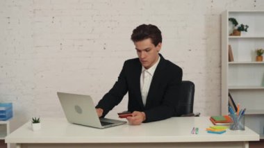 Masada dizüstü bilgisayar kullanan ve elinde kredi kartı olan genç bir adamın internetten alışveriş yaparken çekilmiş orta boy videosu. Bir yemek teslimatı alıyor. Teslimat hizmeti, web sitesi, çevrimiçi alım.
