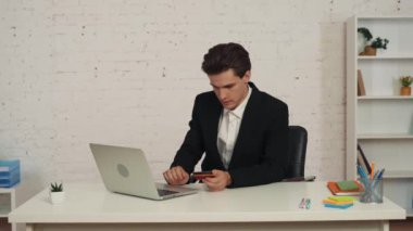 Masada dizüstü bilgisayar kullanan ve elinde kredi kartı olan genç bir adamın internetten alışveriş yaparken çekilmiş orta boy videosu. Bir yemek teslimatı alıyor. Teslimat hizmeti, web sitesi, çevrimiçi alım.