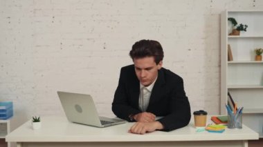 Genç bir adamın laptopun önünde masada otururken, şekerleme yaparken, esnerken, kahvesini yudumlarken ve işine geri dönerken çekilmiş orta boy videosu. İş, aşırı çalışma ve yorgunluk..