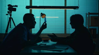 Medium silhouette shot of an perpetrator, prisoner sitting in the interrogation room in front of the detective. The policemnan tries to get the confession. True crime, documentary, creative content. clipart