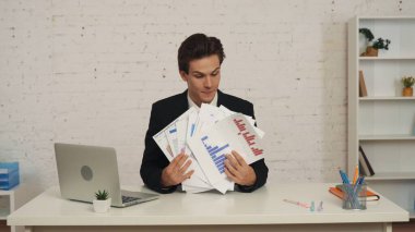 Ofiste oturan genç bir adamın elinde grafikleri ve çizelgeleri gösteren orta boy bir fotoğrafı. Adam onlara bakıyor, mutlu ve memnun. İş, kariyer büyümesi, reklam.