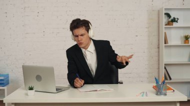 Genç bir adamın ofiste dizüstü bilgisayarıyla çalışırken, kulaklıklardan müzik dinlerken, sandalyede dans ederken ve şarkı söylerken orta boy görüntüsü. Müzik platformları, cihazlar ve teknoloji