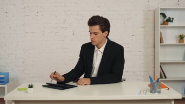 Genç bir adamın masasında otururken orta boy bir fotoğraf, tablet üzerinde çalışırken stil ve kalem kullanırken. Modern teknolojiler, fırsatlar, elektronik cihazlar, reklamlar.