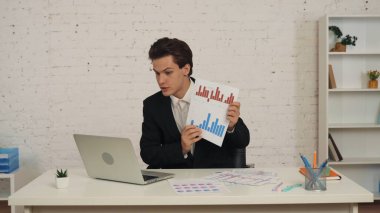 Ofiste dizüstü bilgisayarının önünde oturan genç bir adamın orta ölçekli bir görüntüsü. Konuşuyor, biriyle konuşuyor, grafikler ve chartsy gösteriyor. İş, web kaynakları, uygulama.