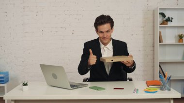 Ofiste oturan genç bir işadamının orta ölçekli bir fotoğrafı. Yemek siparişi, az önce aldığı pizza. O, bir onay veriyor. Kurye hizmetleri, yemek servisi, web sitesi ve uygulama reklamları.