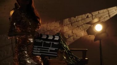 Sinematografi ve sahne arkası yaratıcı konsepti. Yönetmen koltuğunda uzanan birçok film şeritlerinin yakın plan çekimleri, altın elbiseli kadın el çırpma tahtasıyla çerçeveye giriyor..