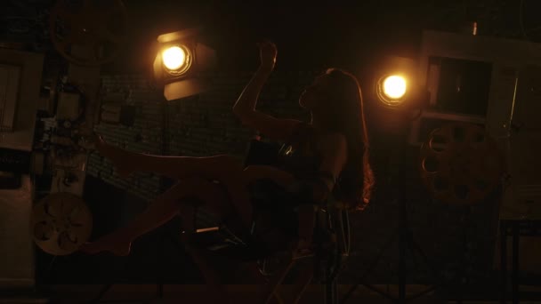 电影摄影和电影舞台为后台创意理念奠定了基础 黑衣黑发女人的轮廓 赤脚坐在导演的椅子上 缠绕着胶卷 摸着她的头发 — 图库视频影像