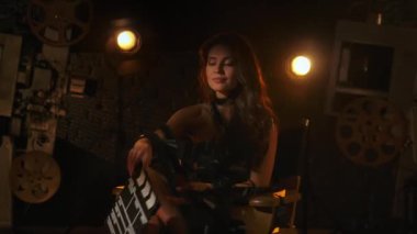 Sinematografi ve sahne arkası yaratıcı konsepti. Siyah elbiseli bir kadının film şeritlerine dolanmış bir şekilde yönetmen koltuğunda oturduğu, elinde tuttuğu ve kapattığı yakın çekim..