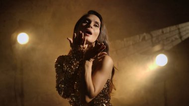 Sinematografi ve sinema sahne arkası reklam yaratıcı konsepti. Altın elbiseli esmer kadının yakın plan çekimi. Stüdyoda tuğla duvara yaslanmış öpüşmesi..