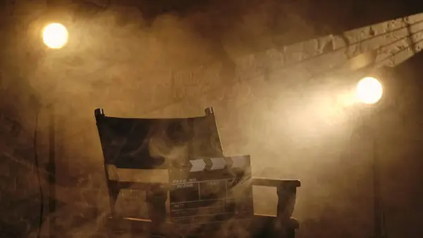 映画と映画の舞台裏広告クリエイティブコンセプト 監督の椅子に立ったクラッパーボードのクローズアップショット バックグラウンドのプロジェクター スタジオで暖かい光と煙 — ストック写真