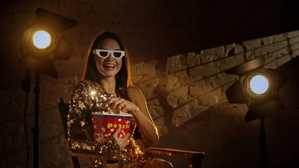 映画と映画の舞台裏広告クリエイティブコンセプト 黄金のドレスのブルネット女性のクローズアップショット 取締役の椅子に座って 3Dメガネを着て バケツからポップコーンを食べる — ストック写真