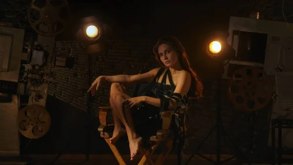 映画と映画の舞台裏広告クリエイティブコンセプト 黒いドレスの魅力的な女性 監督の椅子に座って裸足 彼女の体の上に多くのフィルムストリップ カメラを見て — ストック写真