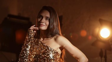 Sinematografi ve sinema sahne arkası reklam yaratıcı konsepti. Altın elbiseli güzel esmer kadın aktrisin yakın plan fotoğrafı. Duvara karşı duruyor ve fotoşop için poz veriyor, gülümsüyor..