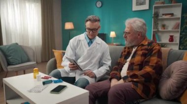 Hastanın evdeki durumunu kontrol eden bir doktorun tam boy videosu. O, sağlık sorunları olan yaşlı bir adama bir şey açıklamak için tablet kullanıyor. Sağlık hizmeti, sağlık hizmeti, reklam.