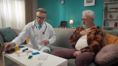 Hastanın evdeki durumunu kontrol eden bir doktorun tam boy videosu. Bir tablet kullanıyor ve sağlık sorunları olan yaşlı bir adama astım ilacı yazıyor. Tıbbi hizmet, reklam..