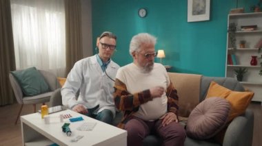 Hastanın evdeki durumunu kontrol eden bir doktorun tam boy videosu. Nefes alışını ve kalp atışlarını incelemek için steteskop kullanıyor. Sağlık sistemi, sağlık hizmetleri, reklam.