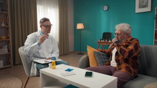 一个医生在家中检查病人病情的全片录像 他正在给一个有健康问题的老年人开药方 保健系统 医疗服务 — 图库视频影像
