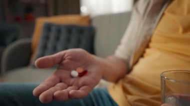 Yakın plan, orta yaşlı bir adamın koltukta, kanepede otururken elinde haplar, elinde ilaçlarla içki içerken çekilmiş detaylı videosu. Uzaklaş. Sağlık, eczane, ilaç reklamları..