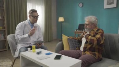 Hastanın evdeki durumunu kontrol eden bir doktorun tam boy videosu. Sağlık sorunları olan yaşlı bir adama reçete yazıyor. Sağlık sistemi, sağlık hizmeti, reklam. HDR