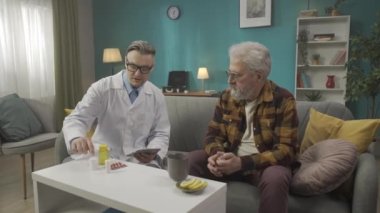 Hastanın evdeki durumunu kontrol eden bir doktorun tam boy videosu. Sağlıkla ilgili sorunları olan yaşlı bir adama ilaç ve hap reçetesi yazıyor. Tıbbi hizmet, reklam.