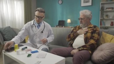 Hastanın evdeki durumunu kontrol eden bir doktorun tam boy videosu. Bir tablet kullanıyor ve sağlık sorunları olan yaşlı bir adama astım ilacı yazıyor. Tıbbi servis, reklam. HDR